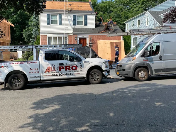 ALL PRO pickup truck and work van parked in front of a two-story home during a roof tear-off