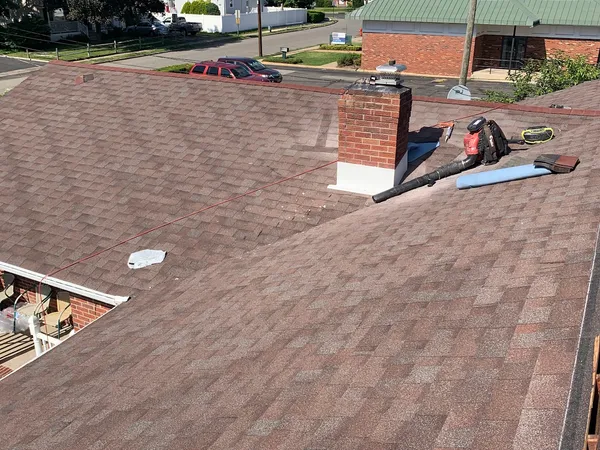 Brown asphalt shingle roof with a brick chimney and a leaf blower left from cleanup