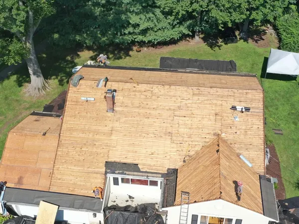 Aerial view of a house with the old roof stripped and new plywood decking installed across every slope