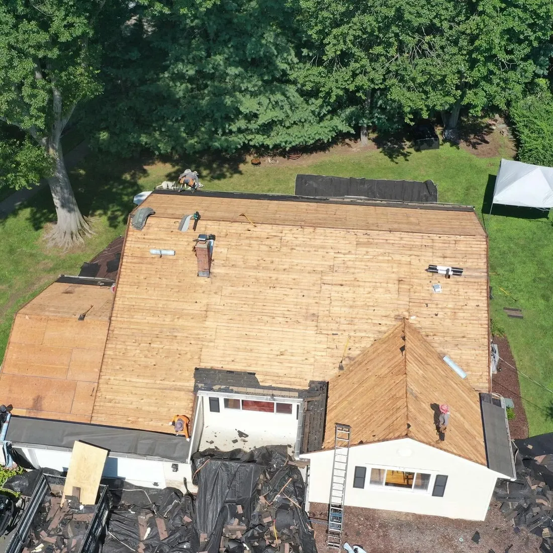 Aerial view of a house with the old roof stripped and new plywood decking installed across every slope