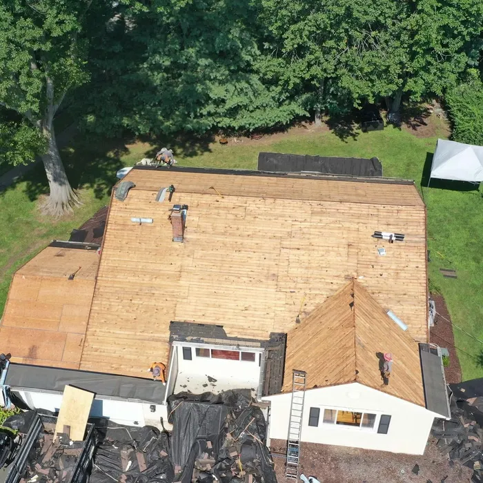 Aerial view of a house with the old roof stripped and new plywood decking installed across every slope