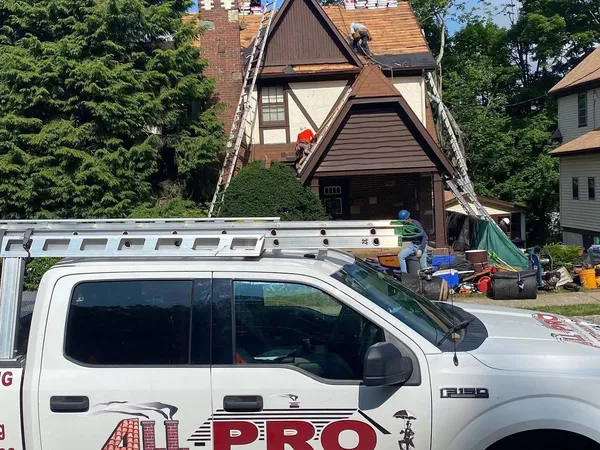 ALL PRO pickup truck parked in front of a Tudor-style home while the crew works on the roof