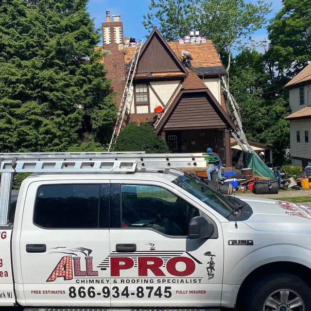 ALL PRO pickup truck parked in front of a Tudor-style home while the crew works on the roof