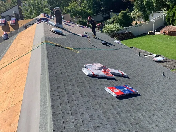 Crew finishing a new charcoal shingle roof, with shingle bundles on the slope and fresh decking at the edge