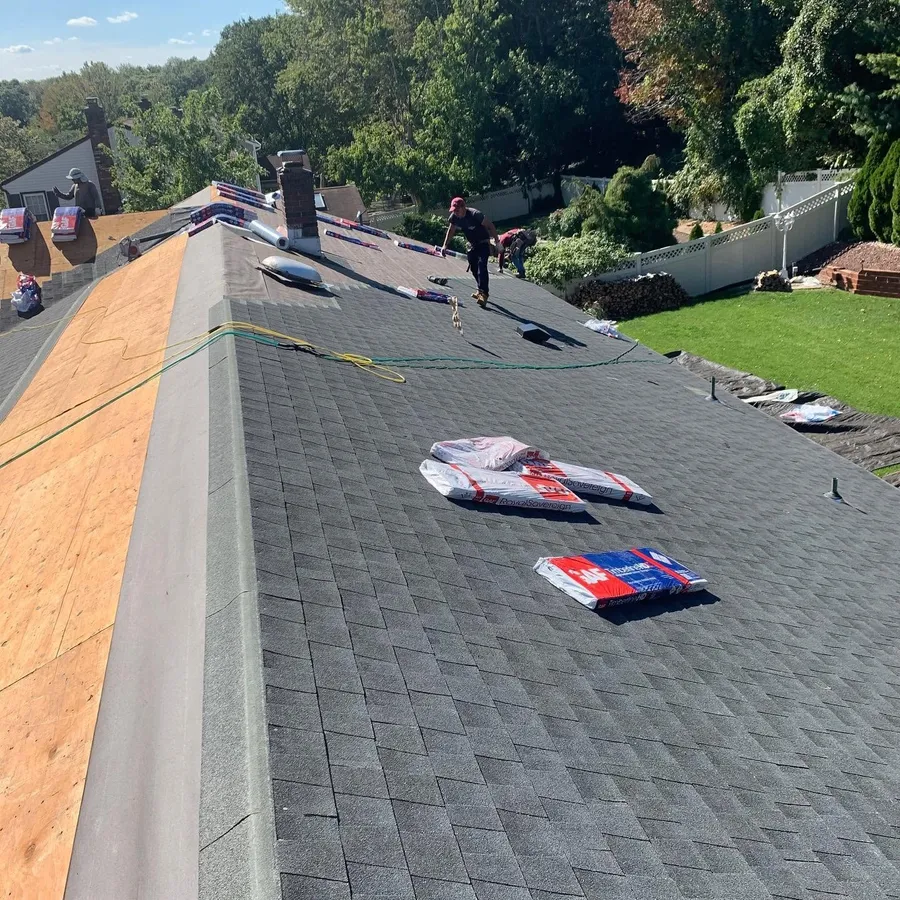 Crew finishing a new charcoal shingle roof, with shingle bundles on the slope and fresh decking at the edge
