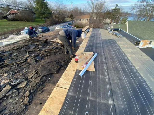 Crew tearing off old shingles on one side of a roof while new decking and underlayment go down on the other