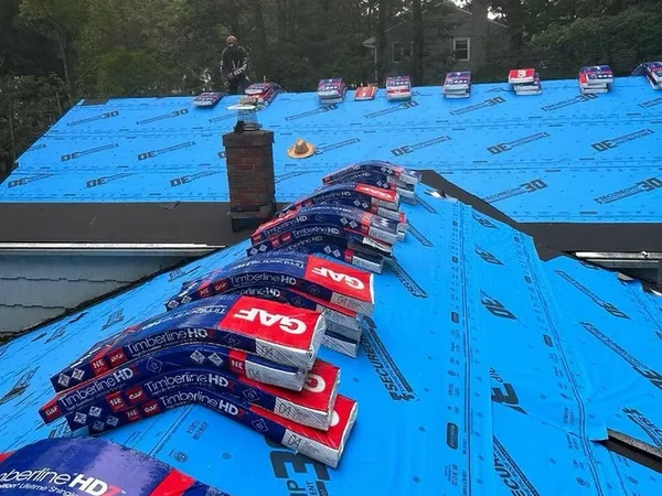 Stacks of GAF Timberline HDZ shingles staged on blue synthetic underlayment across a roof