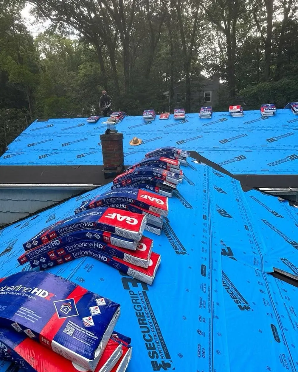 Stacks of GAF Timberline HDZ shingles staged on blue synthetic underlayment across a roof