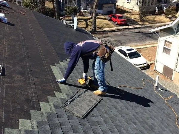Roofer nailing new dark shingles course by course with a nail gun