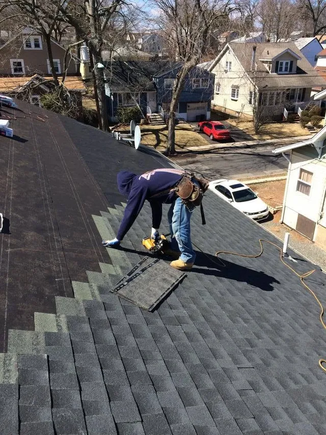 Roofer nailing new dark shingles course by course with a nail gun