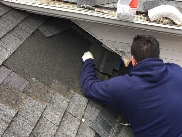Roofer replacing damaged shingles at the roof edge above a gutter