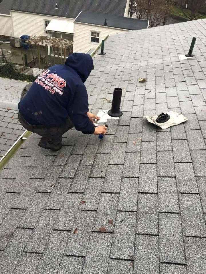 Roofer sealing a new pipe boot on a gray shingle roof