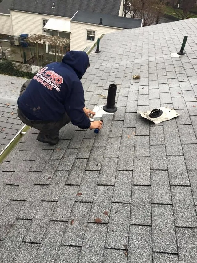 Roofer sealing a new pipe boot on a gray shingle roof