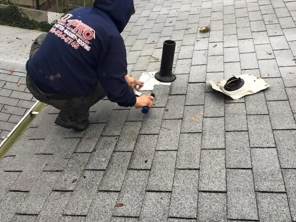 Roofer sealing a new pipe boot on a gray shingle roof