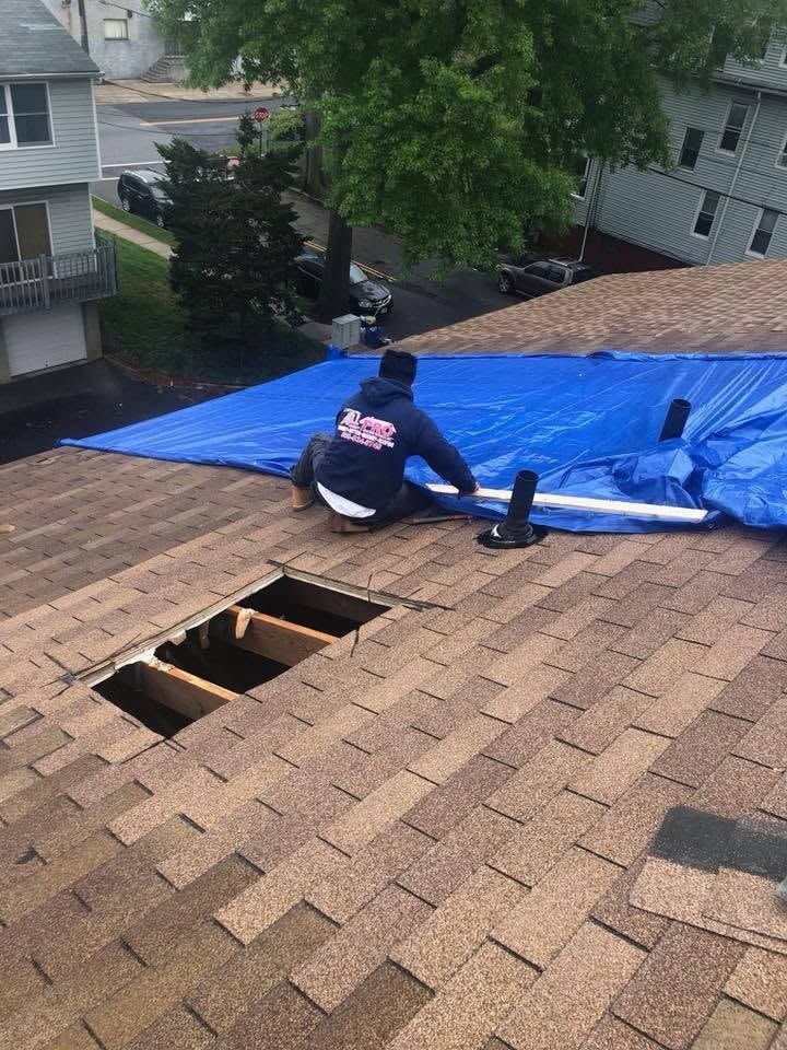 Roofer securing a blue tarp over a damaged section of roof, with open holes in the decking beside him