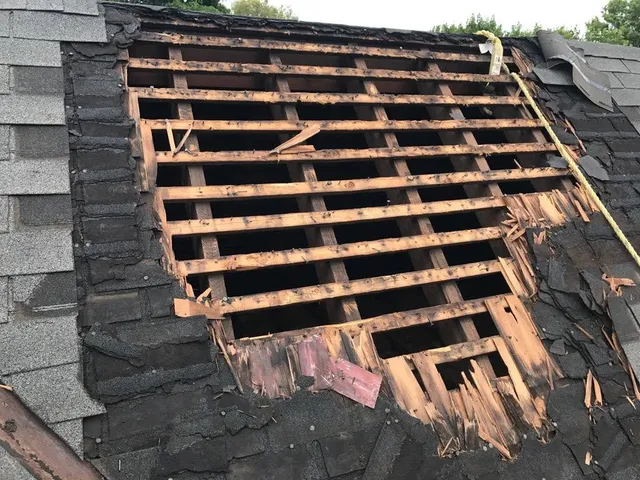 Section of roof with shingles and boards broken away, exposing the roof framing