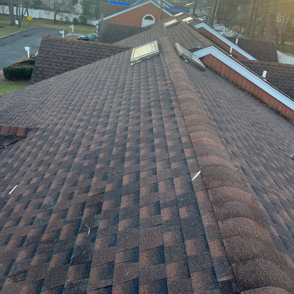 Brown architectural shingle roof with matching ridge caps and skylights along the far slope