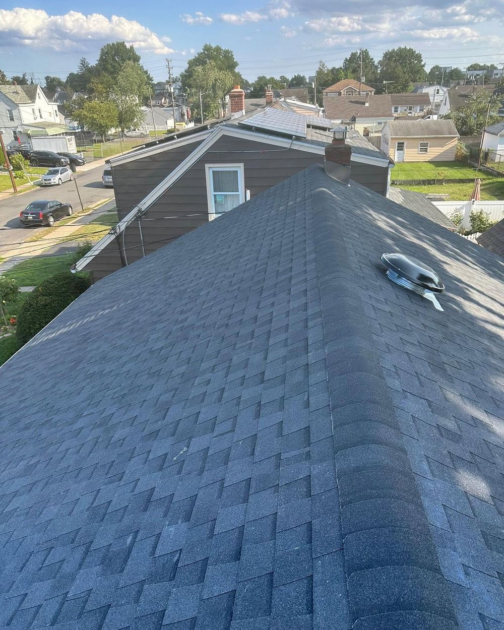 New charcoal shingle hip roof with a round roof vent, seen from above a residential block