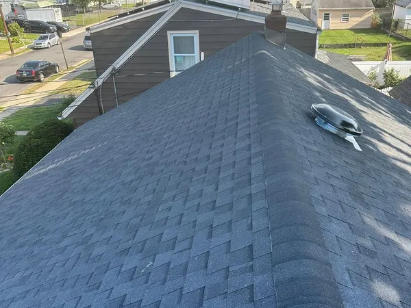 New charcoal shingle hip roof with a round roof vent, seen from above a residential block