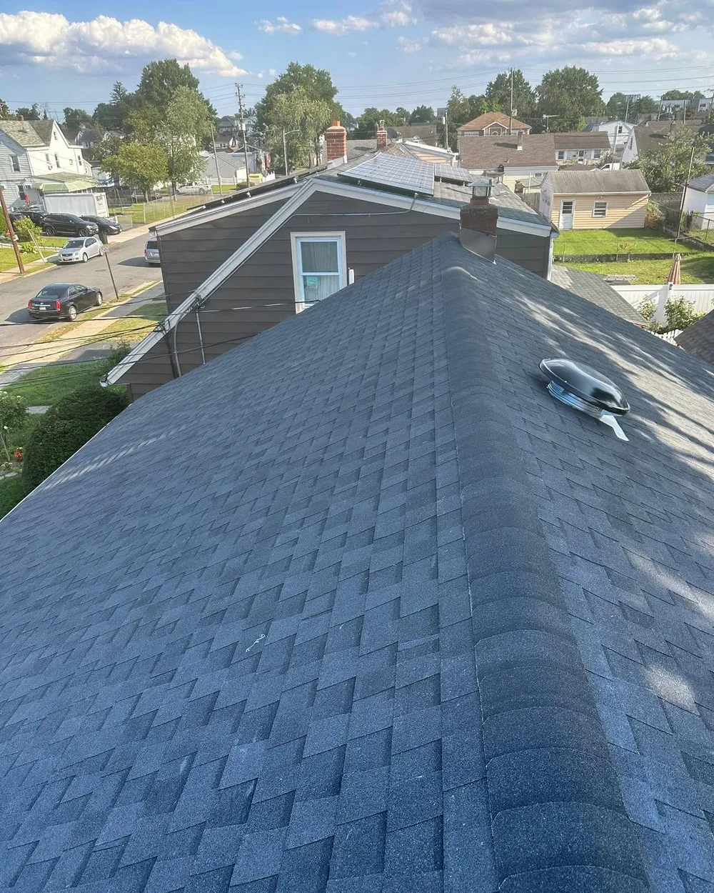 New charcoal shingle hip roof with a round roof vent, seen from above a residential block