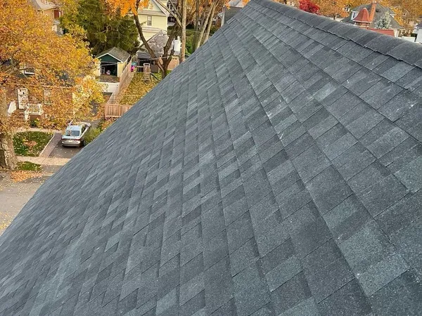 New charcoal shingle roof slope with autumn trees and neighboring houses below