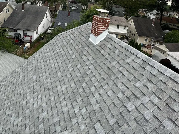 New light-gray shingle roof with a flashed brick chimney, overlooking a neighborhood of older homes