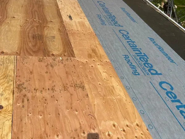 New plywood roof decking with CertainTeed synthetic underlayment being rolled out over it
