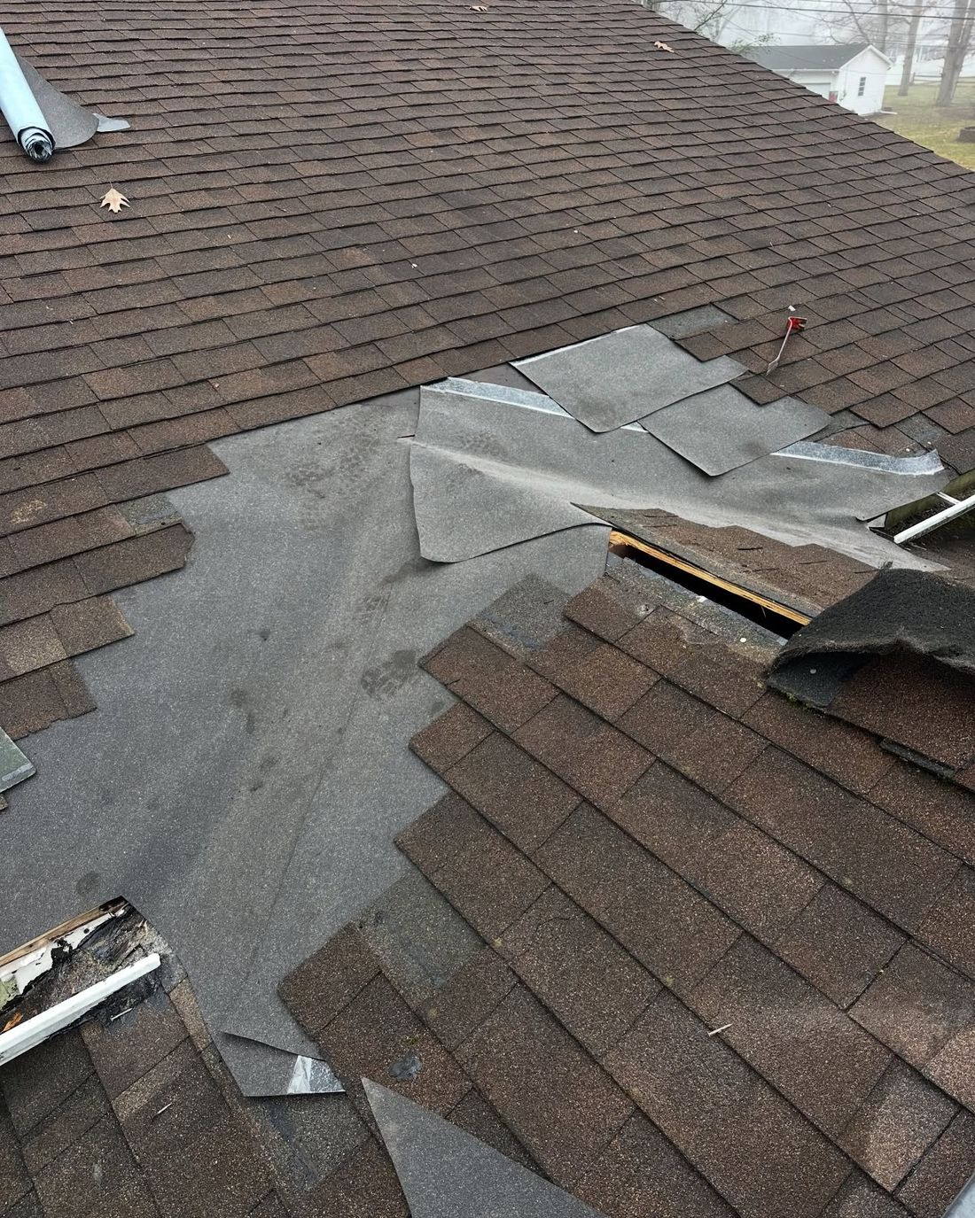 Brown shingle roof opened up for repair, with new underlayment patched in under the shingles