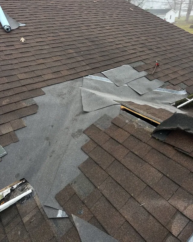 Brown shingle roof opened up for repair, with new underlayment patched in under the shingles