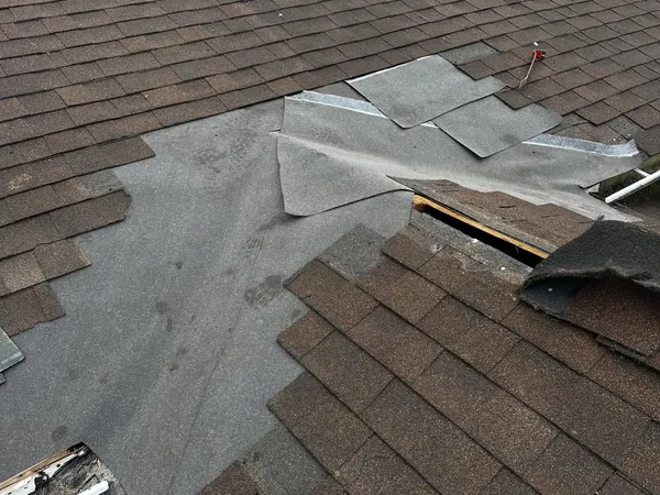 Brown shingle roof opened up for repair, with new underlayment patched in under the shingles