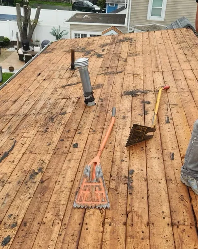 Roof stripped down to old plank boards, with a shingle scraper and a vent pipe, before new decking goes on