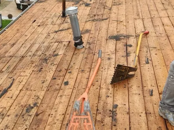 Roof stripped down to old plank boards, with a shingle scraper and a vent pipe, before new decking goes on