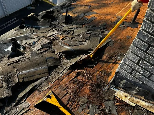 Old shingles and water-damaged decking being torn off next to a chimney