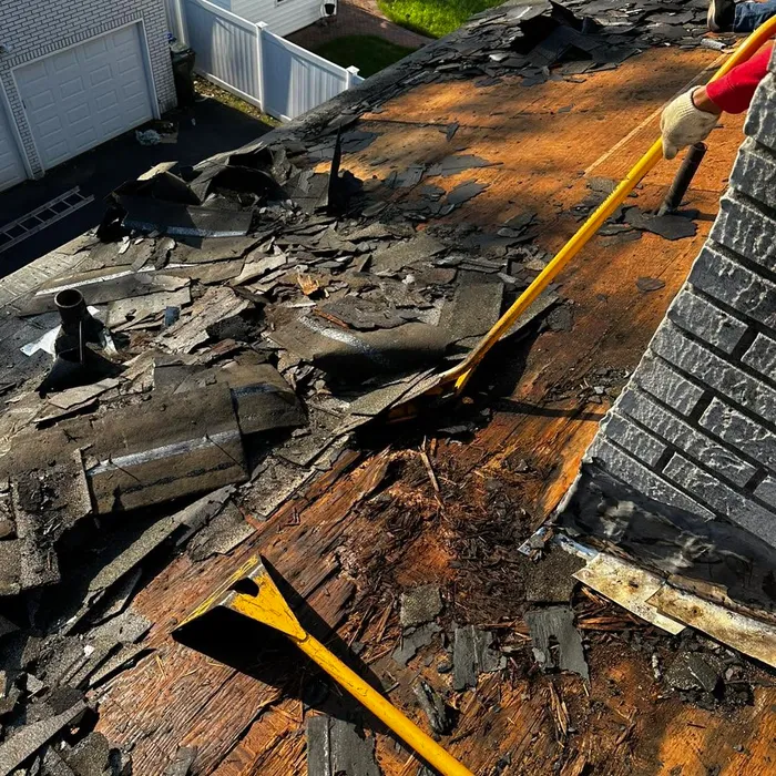 Old shingles and water-damaged decking being torn off next to a chimney