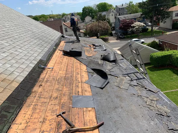 Crew tearing off worn gray shingles down to the old plank roof boards