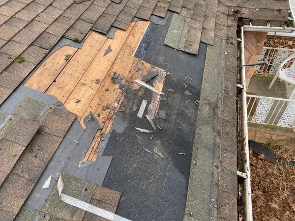 Shingles removed at the roof edge, showing stained, water-damaged decking beneath