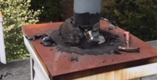 Close-up of a vent pipe with cracked, patched sealant where it meets the roof