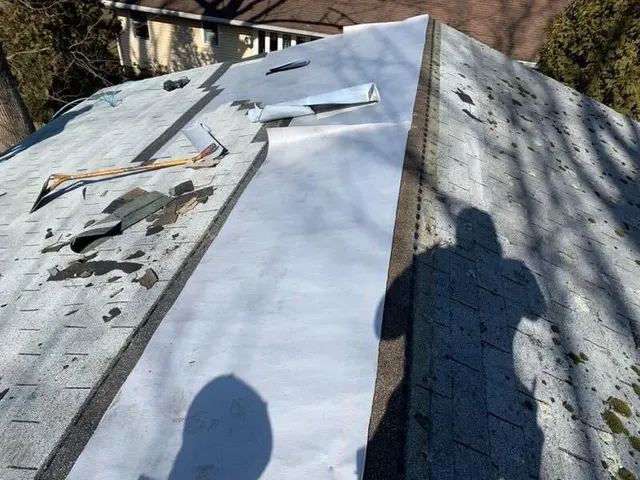 Worn, patchy shingles on one side of a ridge and new white underlayment on the other
