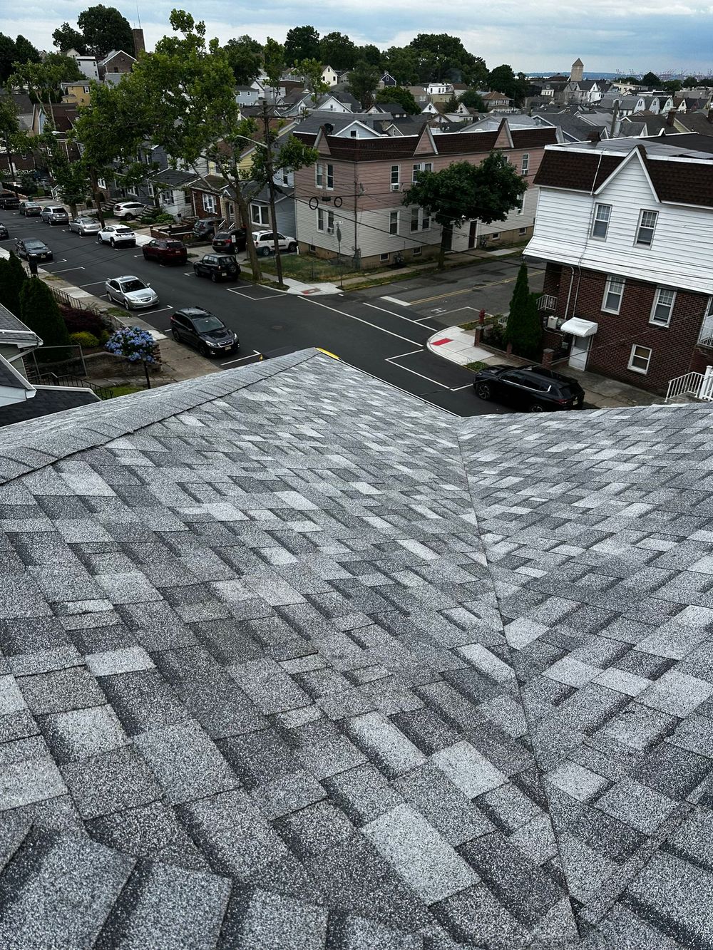 Finished light-gray shingle roof with a clean valley, overlooking a street of row homes
