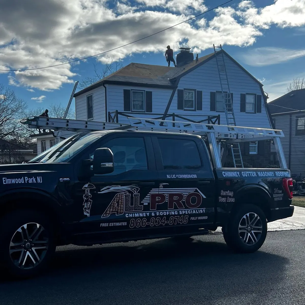 Black ALL PRO pickup truck with a ladder rack parked in front of a house while the crew works on the roof