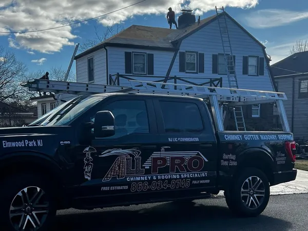 Black ALL PRO pickup truck with a ladder rack parked in front of a house while the crew works on the roof