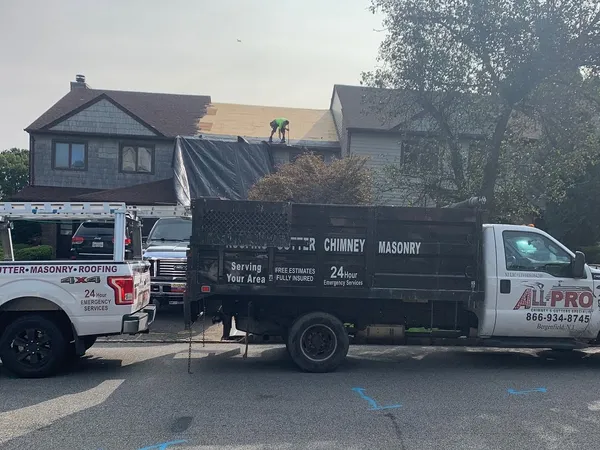 Two ALL PRO trucks parked at a house while a roofer works on the roof