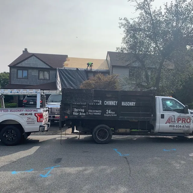 Two ALL PRO trucks parked at a house while a roofer works on the roof