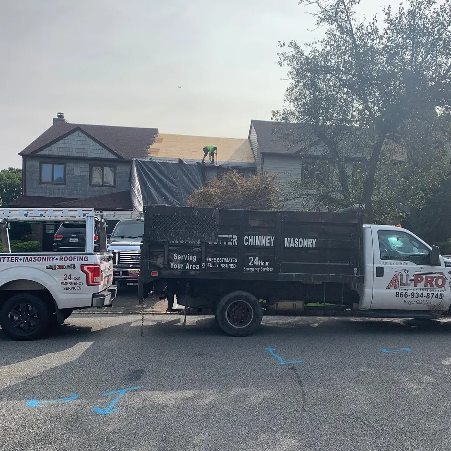 Two ALL PRO trucks parked at a house while a roofer works on the roof
