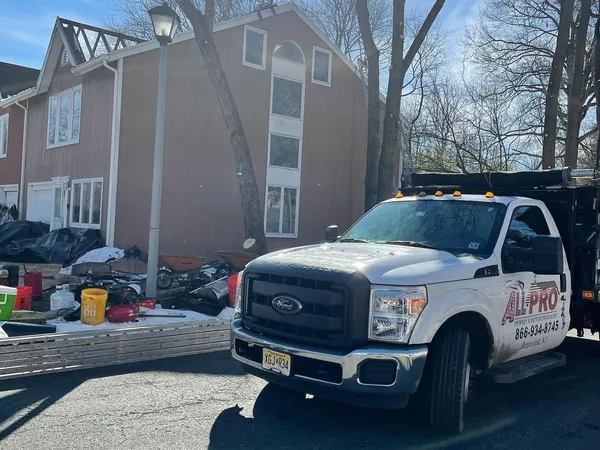 White ALL PRO dump truck parked at a job site beside a two-story home, with tear-off debris in the driveway