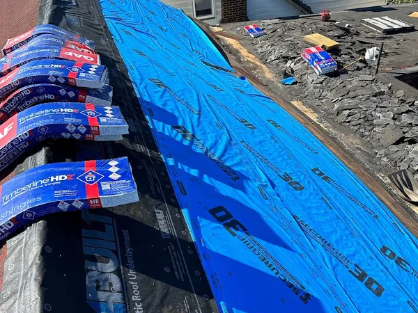 Bundles of GAF Timberline HDZ shingles staged on new blue synthetic underlayment during a roof replacement