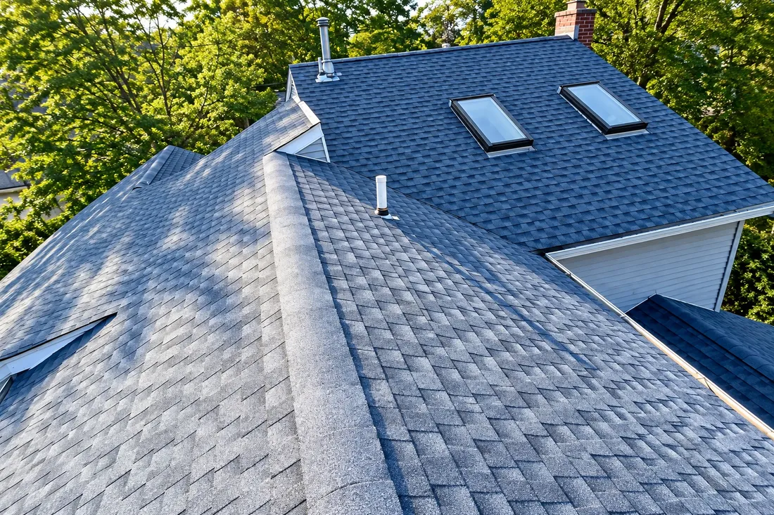 New blue-gray shingle roof with two skylights, a brick chimney, and vent pipes across several roof planes