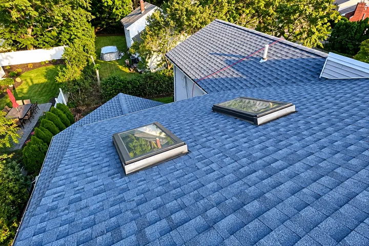 New blue-gray architectural shingle roof with two flashed skylights, overlooking a landscaped backyard