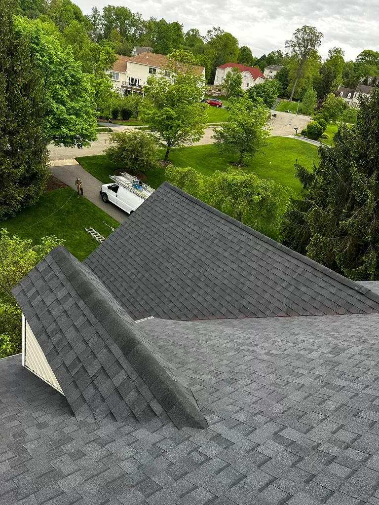 Finished gray asphalt shingle roof with several intersecting ridges and matching ridge caps