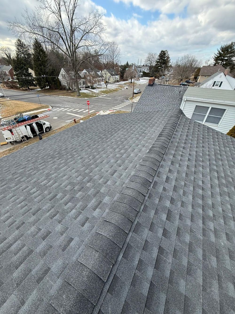 Newly shingled gray roof ridge above a residential street on a cloudy day